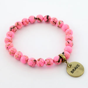 A collection of pink bead bracelets with vintage gold charms featuring words of courage and strength.