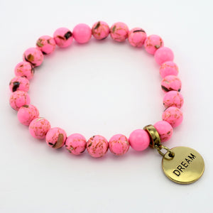 A hot pink bead bracelet with Synthesis Stone, featuring a vintage gold lock bead and word charms, with the word 'brave' visible on one charm.