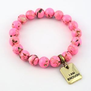 Pink beaded bracelet with a gold tag reading 'I AM ENOUGH' on a white background