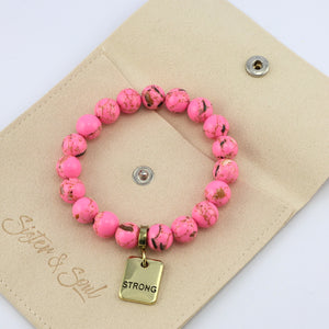 Pink beaded bracelet with a gold tag on a beige pouch, featuring the brand 'Sister & Soul'.