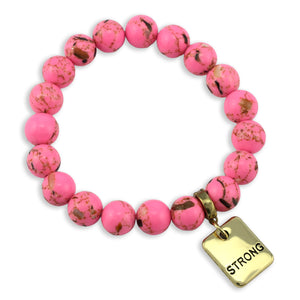Pink beaded bracelet with a gold tag reading 'STRONG' on a white background