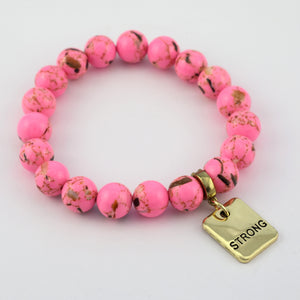 Pink beaded bracelet with a gold tag reading 'STRONG' on a white background