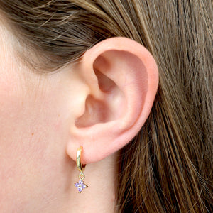 Close-up of an ear wearing a gold earring with a star-shaped purple gem.