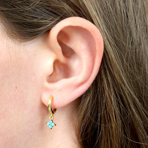 Close-up of an ear wearing a gold hoop earring with a turquoise stone.