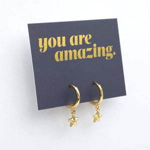 Gold hoop earrings with star charms on a 'you are amazing' card