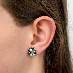 Close-up of an ear wearing a green and gold earring with a white pearl.