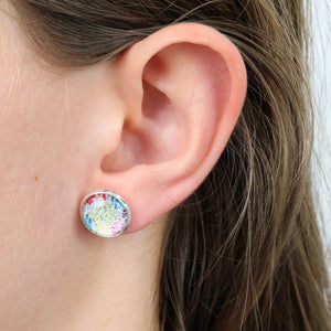 Close-up of an ear wearing a colorful round earring with a blurred background