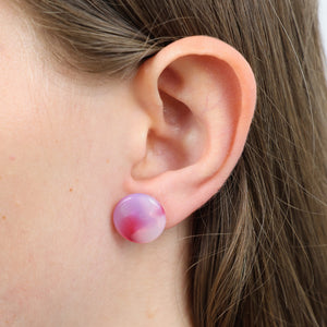A close-up of a person's ear wearing a round stud earring with a pink and white marbled pattern.