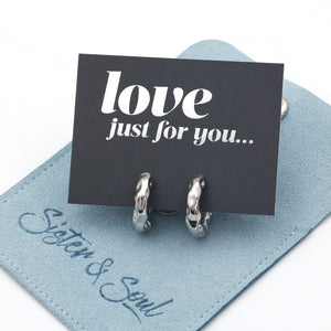 Silver Huggies hoop earrings on a grey card with silver wording that says "love just for you" on top of a blue pouch on a white background