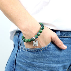 Person wearing a green beaded bracelet with a silver tag on a white background