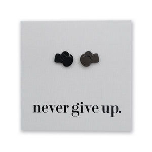 A pair of small boxing glove earrings on a light gray square backing card. , positioned above the printed black text 'never give up.