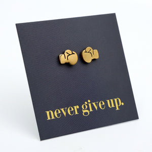 A pair of gold boxing glove stud earrings displayed on a black textured backing card with the phrase 'never give up.' in gold lettering, set against a clean white background.