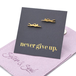 Gold swimmer earrings on a 'never give up' card with a purple jewelry box.