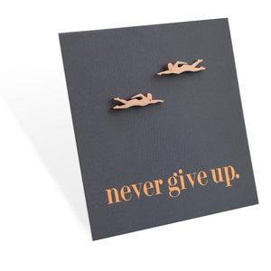 Two small swimming figurine earrings on a dark card with 'never give up' text