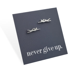 Silver swimmer earrings on a dark gray card with 'never give up.' text