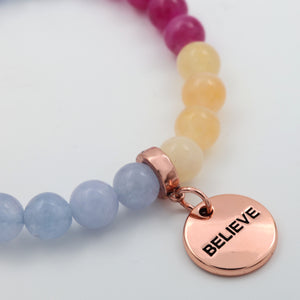 Colorful beaded bracelet with a rose gold 'BELIEVE' charm on a light background