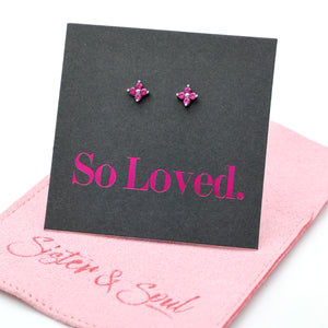 Pink tiny floral star shaped studs presented on a grey card with pink 'So Loved' writing sitting on a pink pouch with 'Sister & Soul' writing.