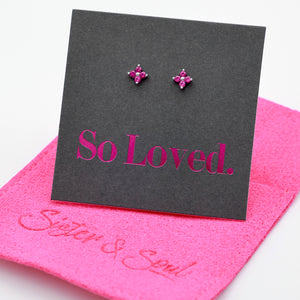 Pink tiny floral star shaped studs presented on a grey card with pink 'So Loved' writing sitting on a hot pink pouch with 'Sister & Soul' writing.