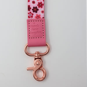 Pink lanyard with floral pattern and rose gold clasp on a light gray background
