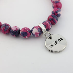 Bracelet with pink and purple beads and a silver 'INSPIRE' charm on a white background