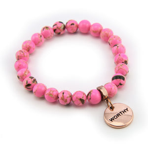 Pink beaded bracelet with a 'WORTHY' charm on a white background