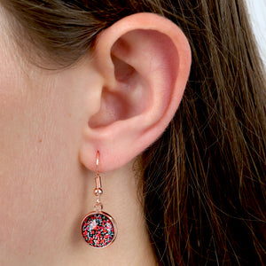 Close-up of an ear wearing a rose gold earring with a colorful gemstone.