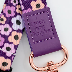 Purple strap with floral pattern and 'teach love inspire' text, featuring a rose gold keychain.