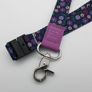 Teach Love Inspire embossed on a navy floral lanyard with purple trim and a lobster clasp.