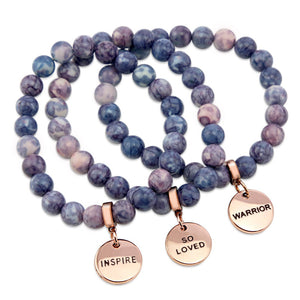 Two bracelets with purple and storm patch agate stone beads and rose gold word charms, one with 'INSPIRE' and the other with 'WARRIOR'.