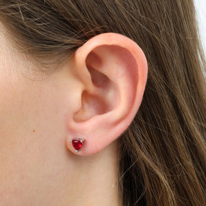 Close-up of an ear wearing a heart-shaped red earring.