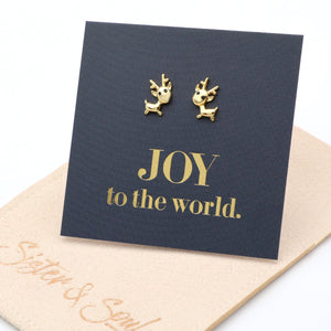 Gold reindeer earrings on a navy card with 'JOY to the world.' text, on a beige surface.