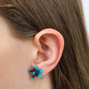 Close-up of an ear wearing a blue star-shaped earring with brown hair.