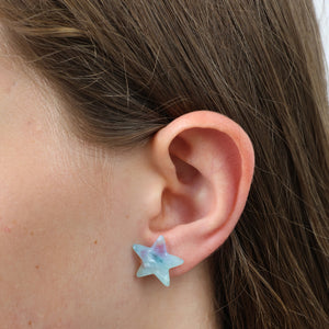 Star-shaped earring worn on a person's ear with a neutral background