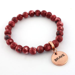 Red beaded bracelet with a 'BRAVE' charm on a white background