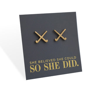 Gold stainless steel hockey earrings on a grey card with 'She believed she could so she did' text