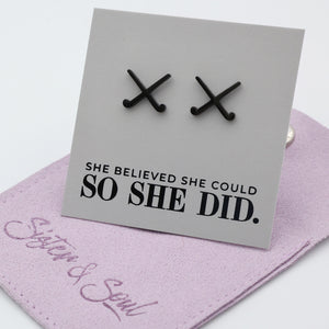 Black stainless steel hockey-shaped earrings on a card with 'She believed she could so she did' text, displayed on a purple gift pouch.