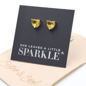 Heart-shaped yellow gemstone earrings on a card with 'She leaves a little sparkle' text.