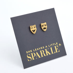 Gold theater mask earrings on a dark gray card with 'She Leaves a Little Sparkle' text.