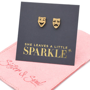 Gold theater mask earrings on a 'She Leaves a Little Sparkle' card with a pink box in the background.
