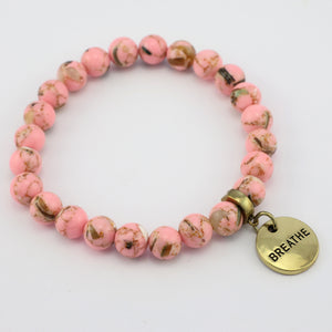 Pink beaded bracelet with a gold 'BREATHE' charm on a white background