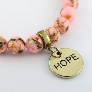 Bracelet with pink beads and a gold 'HOPE' charm on a white background
