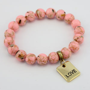 Pink beaded bracelet with a gold 'LOVE' charm on a light gray background