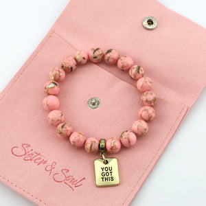 Pink beaded bracelet with gold 'You Got This' charm on a pink pouch with 'Sister & Soul' branding.