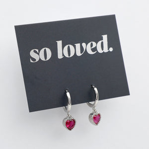 Pink heart shaped huggies dangle earrings presented on a grey card with silver 'so loved' writing.