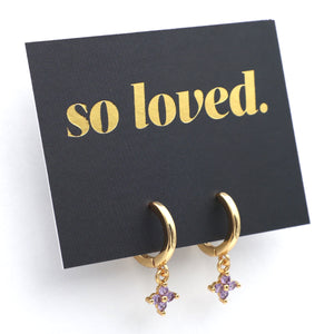 Gold hoop earrings with purple heart charms on a black card with 'so loved.' text.