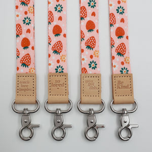 Strawberry Patch lanyards showing Be Kind, Teach Love Inspire, You Got This and So Loved embossed trims and lobster clasps.