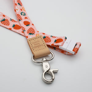 Teach Love Inspire embossed on a pink strawberry and flower lanyard with tan trim and a lobster clasp.