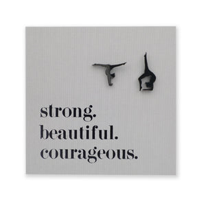 Black stainless steel gymnastics figure shaped earrings on a grey card with 'strong. beautiful. courageous.' text