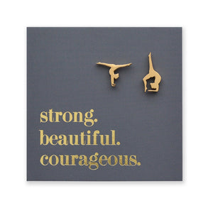 Gold gymnastics pose earrings on a dark gray card with 'strong. beautiful. courageous.' text.