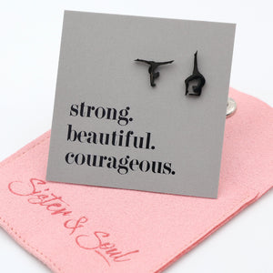 Black stainless steel gymnastics earrings on a gray card with 'strong. beautiful. courageous.' text, on a pink gift pouch background.